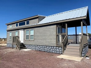 A two-story cabin with a stone foundation, a metal roof, and a wooden deck. - Modern Tiny Home Escape with Scenic Views & Outdoor Lounge in Williams, Arizona (Williams)