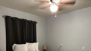 Ein Hotelzimmer mit Bett, Deckenventilator, Nachttisch und Wandsteckdose.