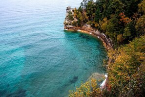 A coastal landscape with clear turquoise waters, rocky cliffs, and autumn foliage.