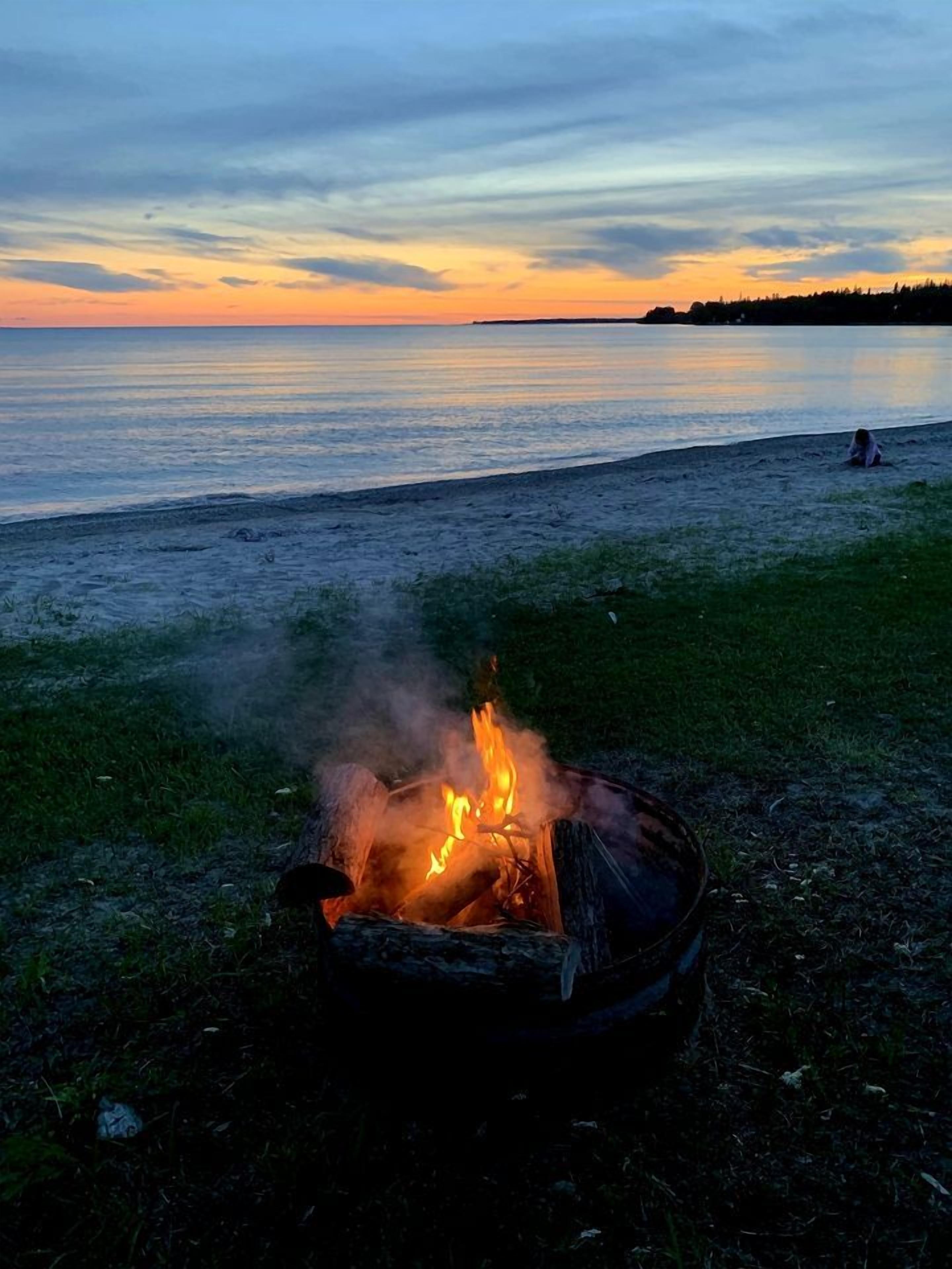 A campfire on a beach with a sunset in the background.