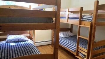 Camas individuales superpuestas con ropa de cama a rayas, estructura de madera y ventana que proporciona luz natural.