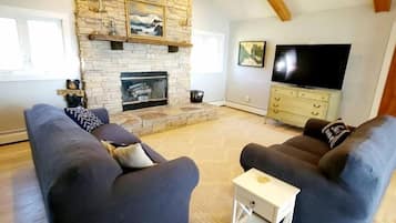 Una sala de estar con chimenea de piedra, dos sofás, un televisor y vigas de madera en el techo.