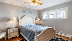 A bedroom with a bed, nightstands, a ceiling fan, a window, and a rug. - Beautiful Lakefront Cottage with Fire Pit in St. Ignace, Michigan (St. Ignace)