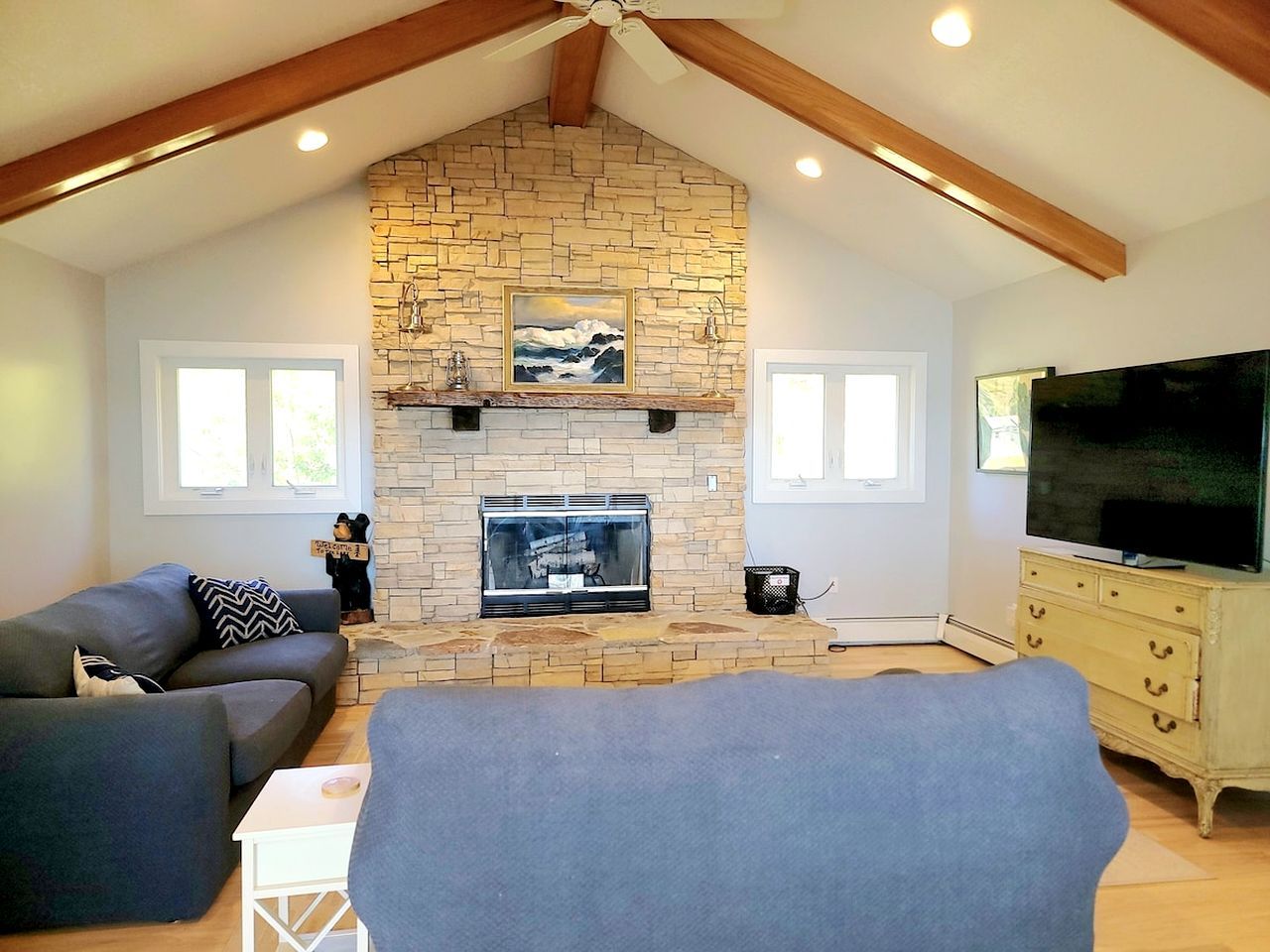 A living room with a stone fireplace, a sofa, a television, and a ceiling fan.