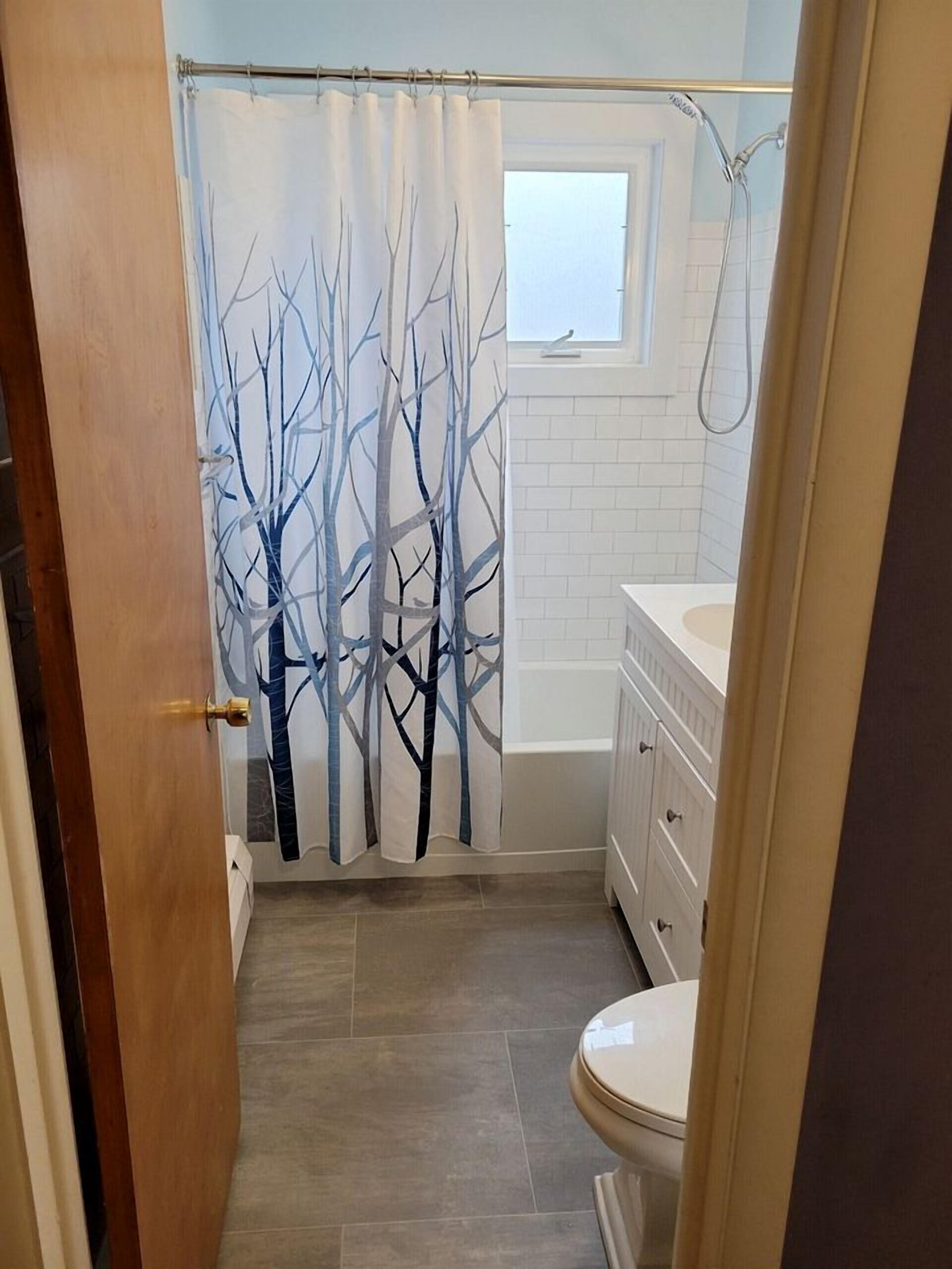 A bathroom with a shower curtain, a window, a bathtub, and a toilet.