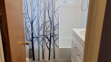 A bathroom with a shower curtain, a window, a bathtub, and a toilet.
