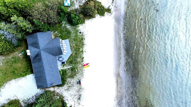 An aerial view of a beach house with a dark roof, a small deck, and a red and yellow flag.