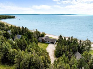 A coastal property with a house surrounded by dense forest, a beach, and a large body of water. - Beautiful Lakefront Cottage with Fire Pit in St. Ignace, Michigan (St. Ignace)