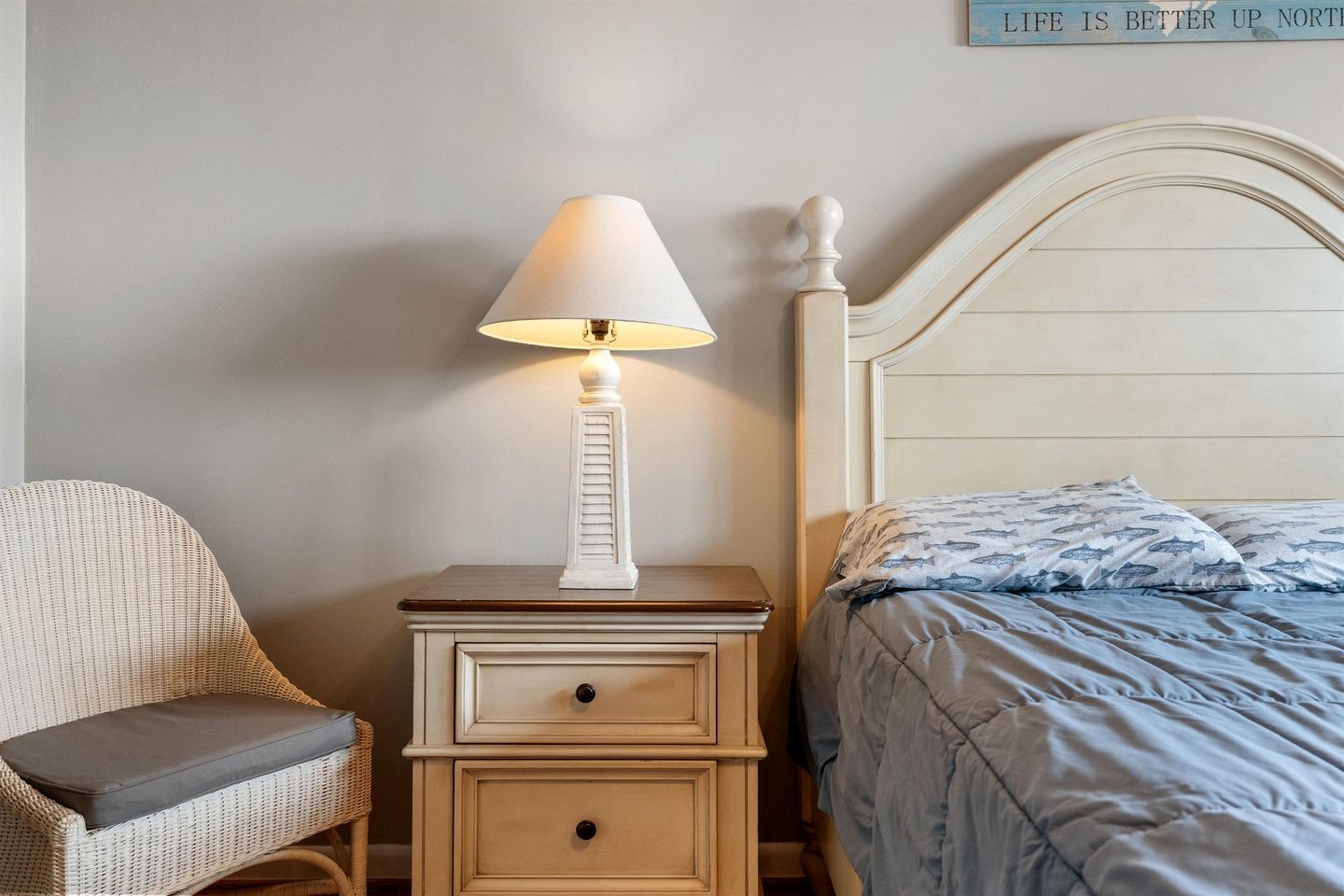 A bedroom with a bed, a nightstand with a lamp, a chair, and a wall with a sign.