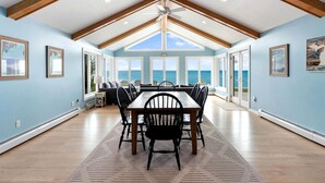 A dining area with a table and chairs, large windows, and a view of the ocean. - Beautiful Lakefront Cottage with Fire Pit in St. Ignace, Michigan (St. Ignace)
