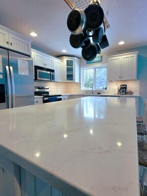 A kitchen with white cabinets, a large island, stainless steel appliances, and hanging pots. - Beautiful Lakefront Cottage with Fire Pit in St. Ignace, Michigan (St. Ignace)