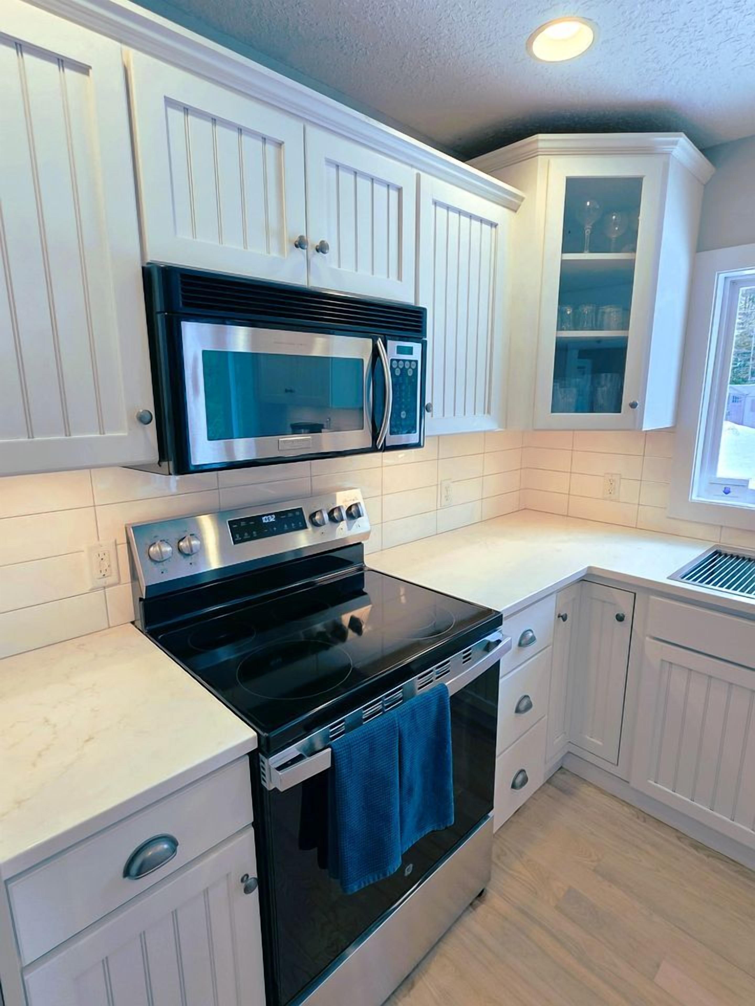 Una cocina con muebles blancos, horno de acero inoxidable, microondas y ventana con vistas.