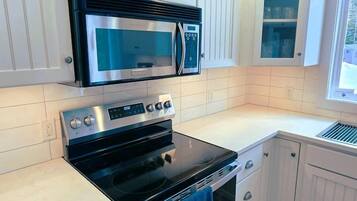 Una cocina con muebles blancos, horno de acero inoxidable, microondas y ventana con vistas.