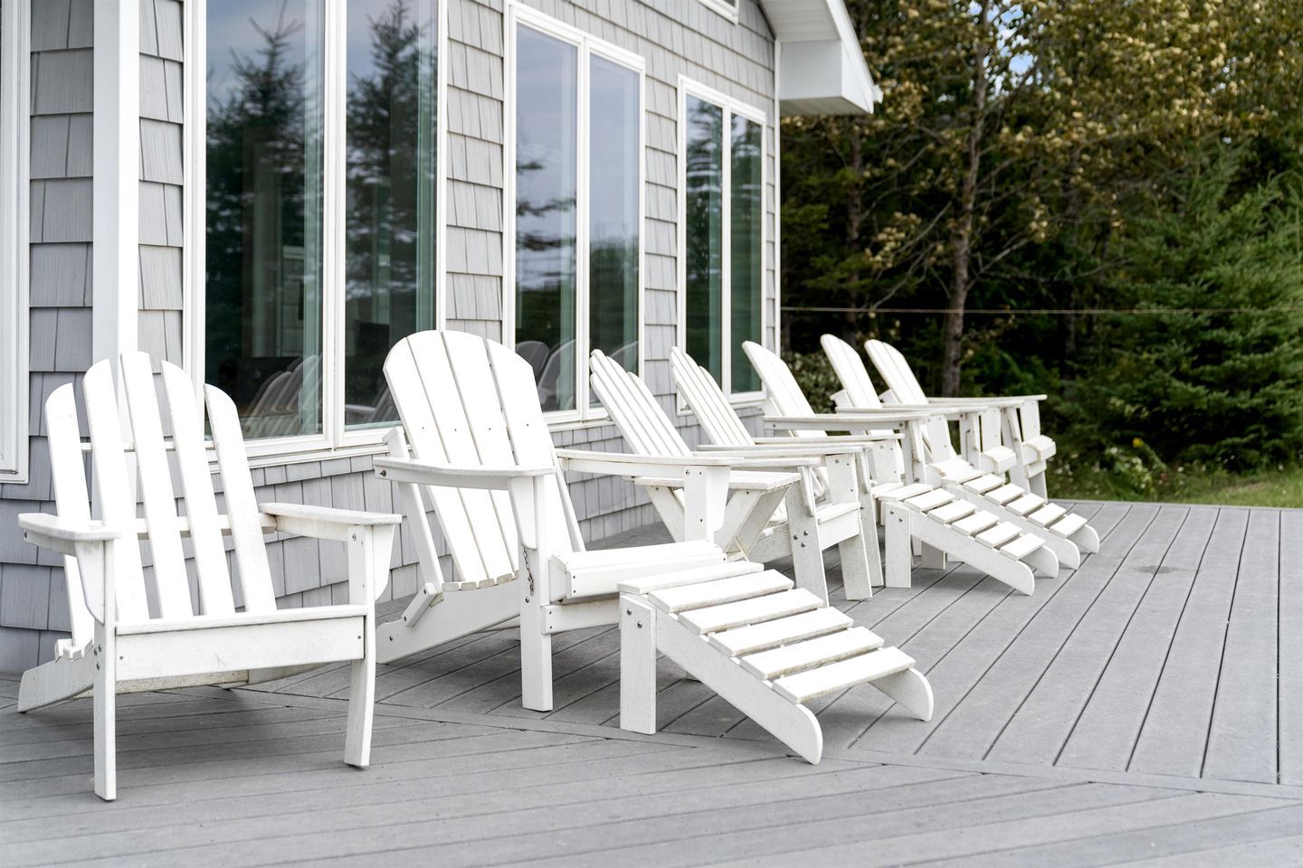 Een terras met witte Adirondack-stoelen en een huis met grote ramen.