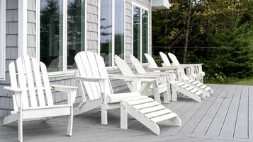 Een terras met witte Adirondack-stoelen en een huis met grote ramen.