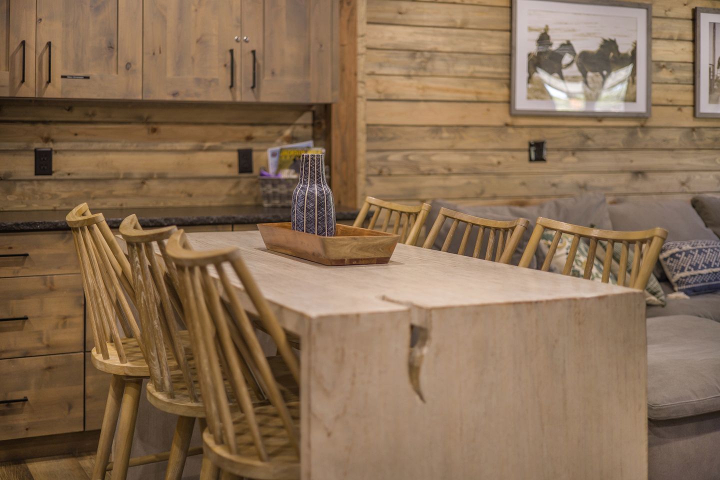A wooden dining table with chairs, a vase, and a framed picture on the wall.