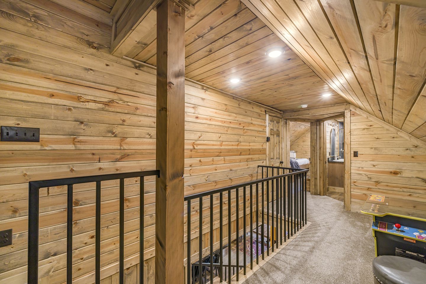 A wooden interior with a sloped ceiling, a metal railing, and a carpeted floor.