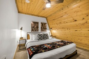 Ein Schlafzimmer mit Holzbalkendecke, einem Bett mit weißer Bettwäsche, zwei Wandlampen und zwei gerahmten Bildern.