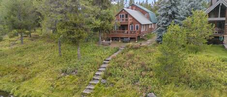 Una cabaña con terraza, rodeada de un bosque frondoso y un arroyo pequeño.