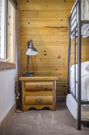 Ein Stockbett mit einem Holztisch und einer Lampe in einem Zimmer mit Holzwänden.