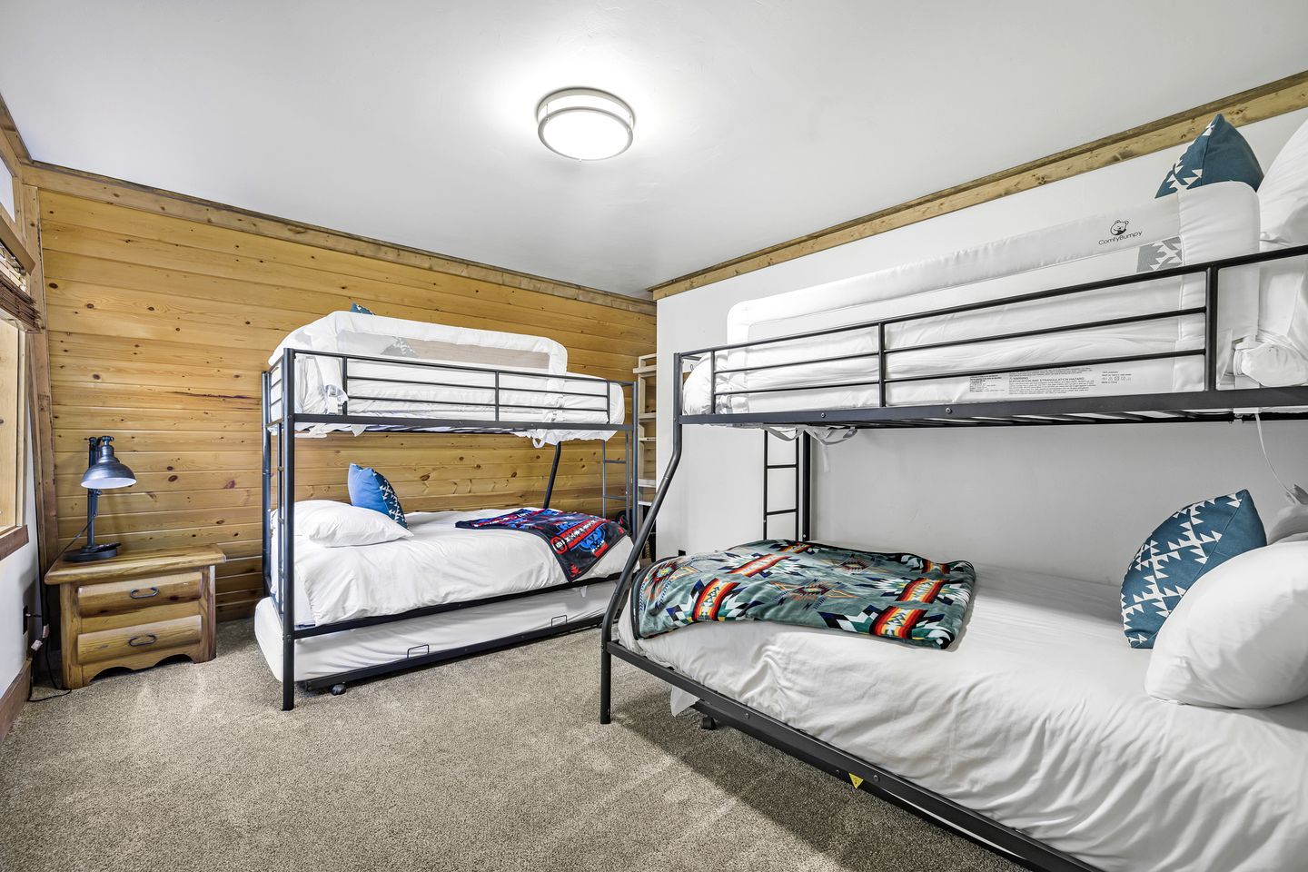 Habitación con literas, pared de madera, escritorio con lámpara y literas con ropa de cama estampada.