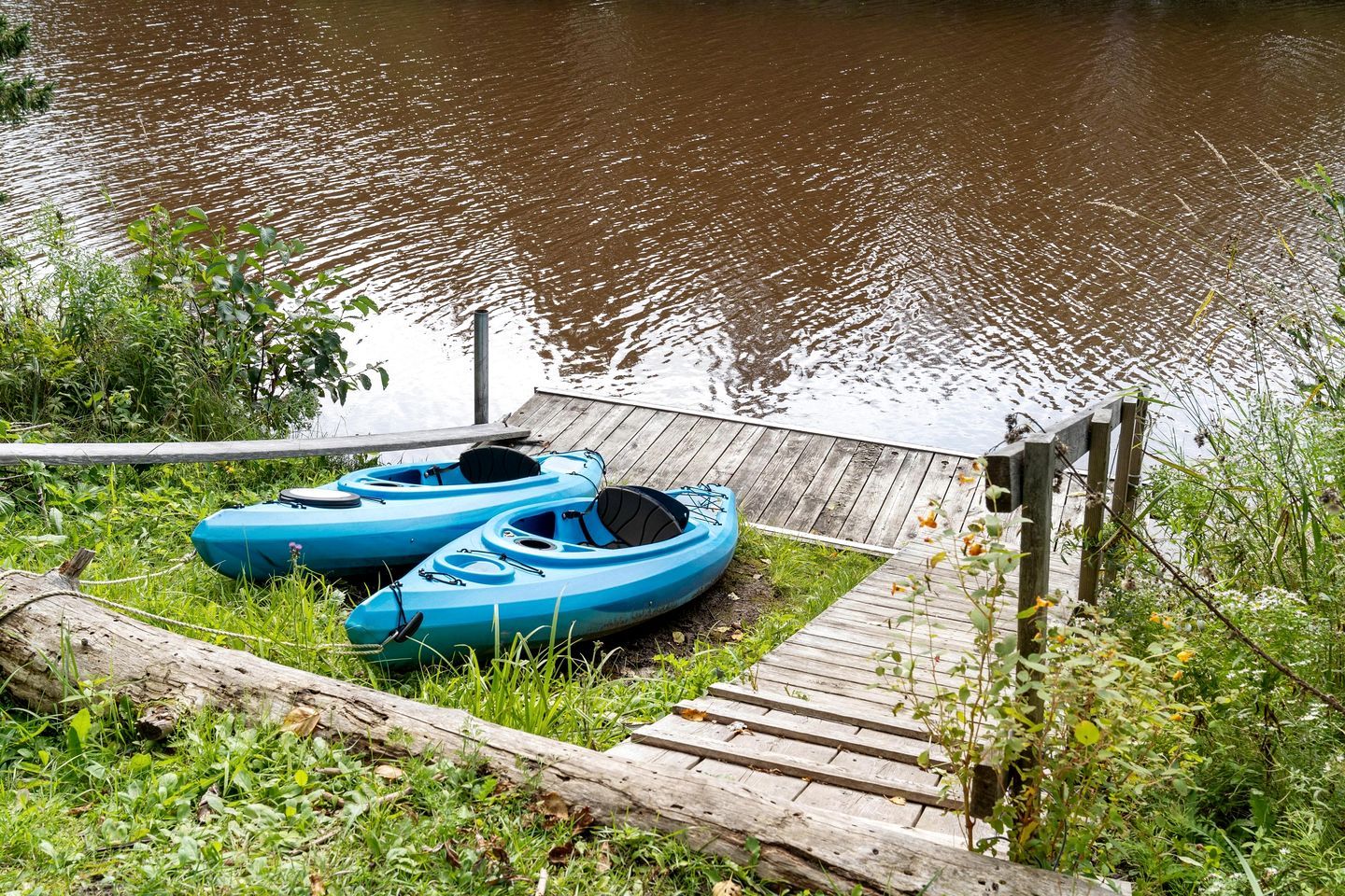 Une jetée en bois avec deux kayaks et une zone herbeuse au bord d’une étendue d’eau calme.