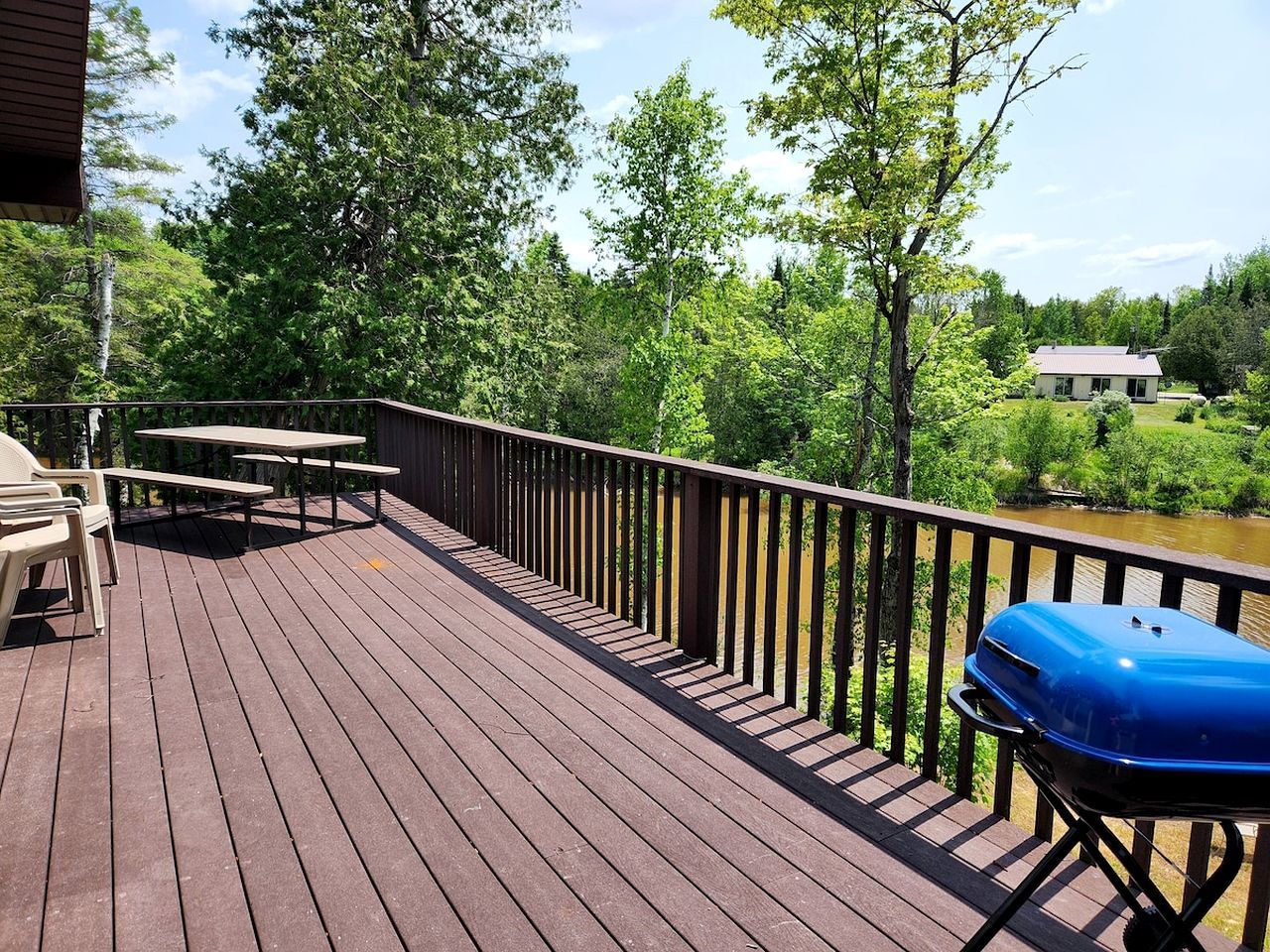 Een houten terras met picknicktafels en een barbecue, omringd door weelderige begroeiing en een waterpartij.
