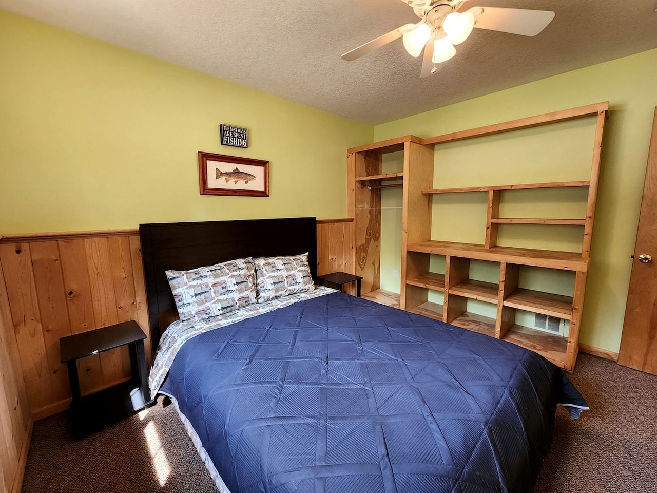 Une chambre à coucher avec un lit, une tête de lit en bois, un ventilateur de plafond et des étagères intégrées.