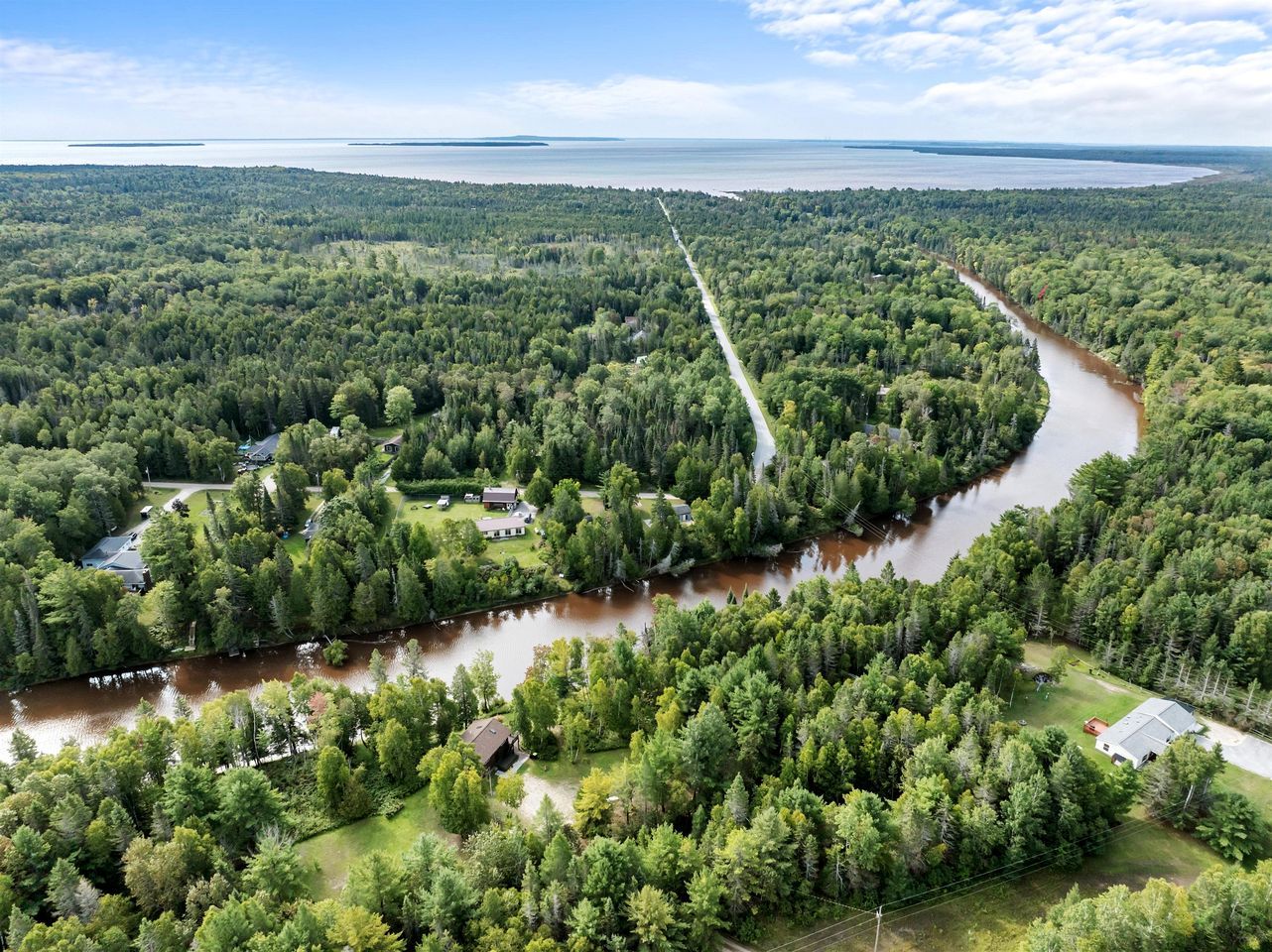 Vista aérea de una zona boscosa con un río sinuoso, casas y cielo despejado.