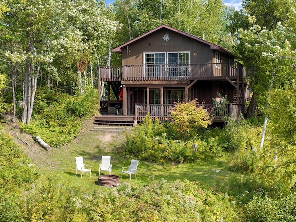 A cabin with a deck, surrounded by trees and greenery.