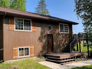 A two-story wooden house with a front porch, a staircase, and a small deck.