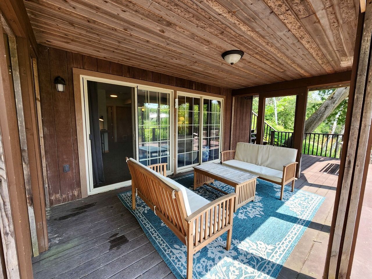 A covered outdoor seating area with a wooden bench, a sofa, and a table.