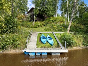A wooden dock with kayaks and a house in the background. - Riverfront Cabin Incredible for Outdoor Enthusiasts with Kayaks in Hessel, Michigan (Hessel)