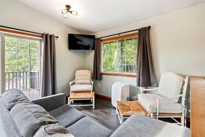 A living room with a sofa, two chairs, a TV, and large windows with curtains.