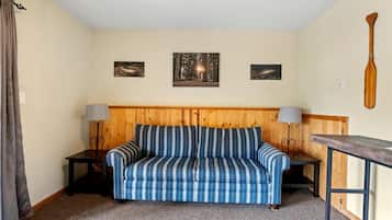 Ein Zimmer mit einem gestreiften Sofa, zwei Nachttischen mit Lampen, einem Holzkopfteil und drei gerahmten Bildern an der Wand.