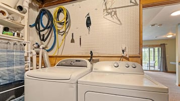 Een wasserette met twee gestapelde wasmachines en drogers, een steigerhouten paneel met verschillende gereedschappen, en een uitzicht op de buitenlucht door een groot raam.
