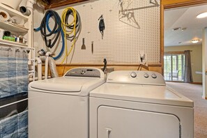 A laundry room with two stacked washers and dryers, a pegboard with various tools, and a view of the outdoors through a large window. - Riverfront Cabin Incredible for Outdoor Enthusiasts with Kayaks in Hessel, Michigan (Hessel)