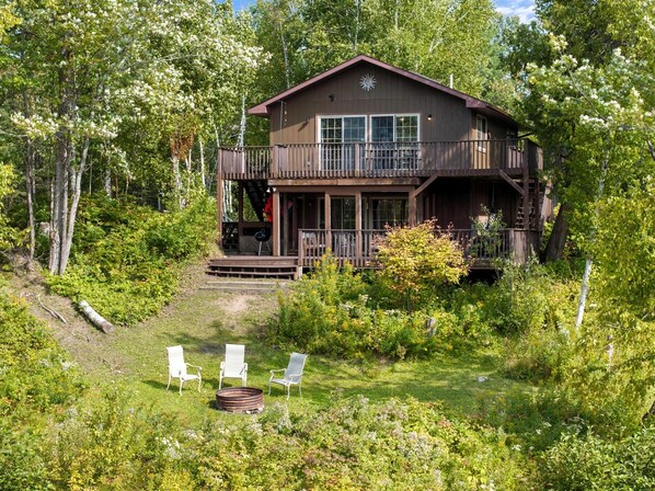 A cabin with a deck, surrounded by trees and greenery.