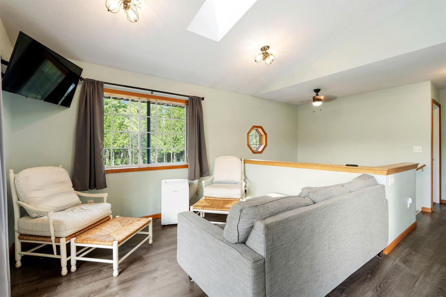 Ein Zimmer mit einer Couch, zwei Sesseln, einem Fernseher, einem Fenster mit Vorhängen, einem Deckenventilator und einem kleinen Tisch.