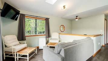 Ein Zimmer mit einer Couch, zwei Sesseln, einem Fernseher, einem Fenster mit Vorhängen, einem Deckenventilator und einem kleinen Tisch.