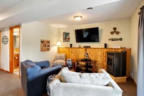 Ein Wohnzimmer mit Fernseher, Kamin, Sofa, Sessel und Lampe.