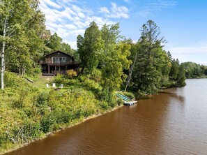 A cabin by a river with a dock, surrounded by trees.