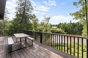 Una terraza de madera con una mesa y bancos que da a un río y una zona boscosa.