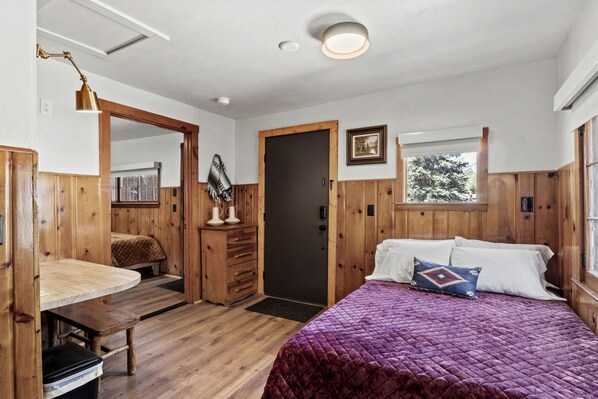 Una habitación con cama, escritorio, cómoda y ventana con vista a árboles.