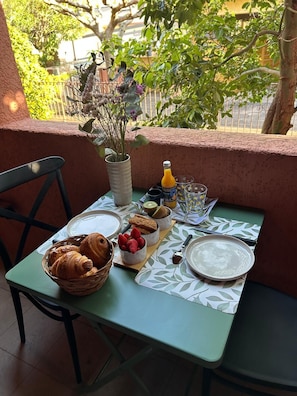Une table dressée avec des croissants, des fraises et une bouteille de jus d’orange, agrémentée d’un vase de fleurs et offrant une vue sur la verdure.
