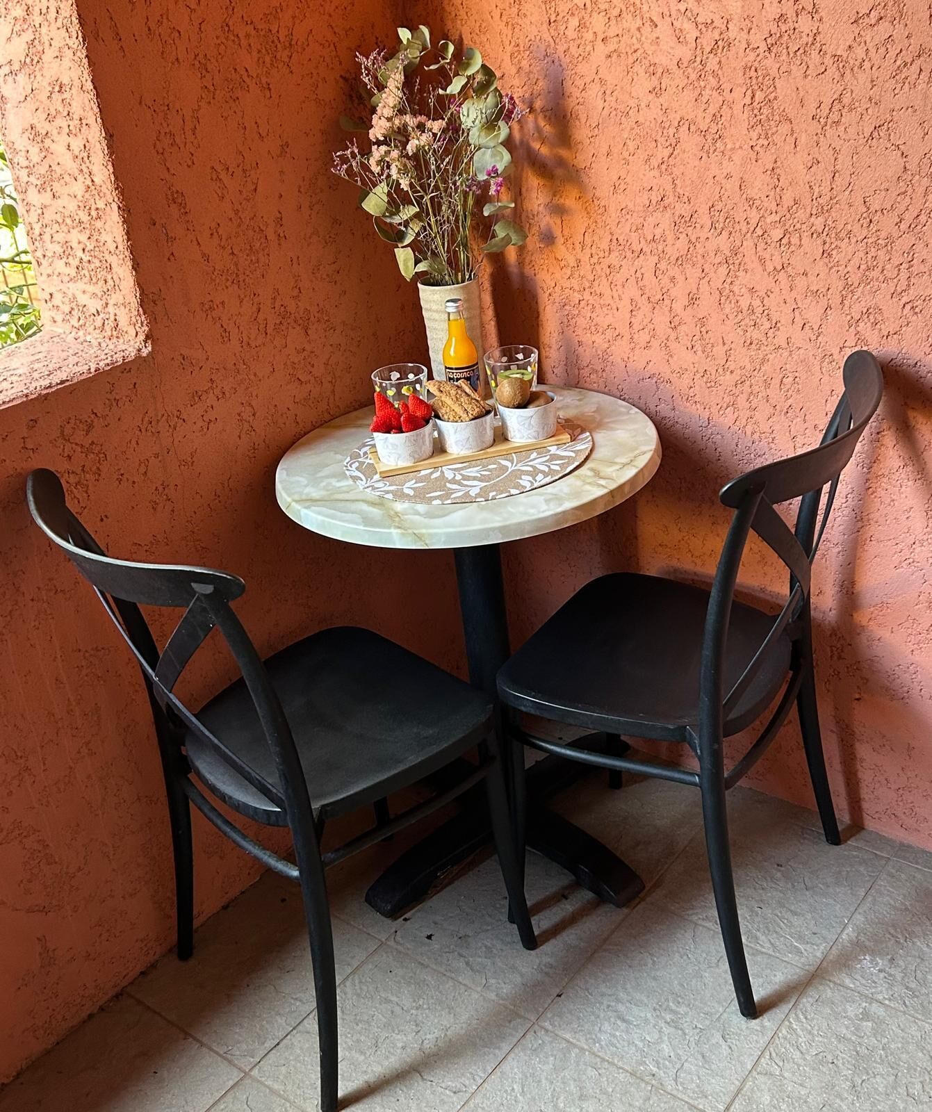 A small round table with two chairs, a vase with dried flowers, and a bottle of orange juice.