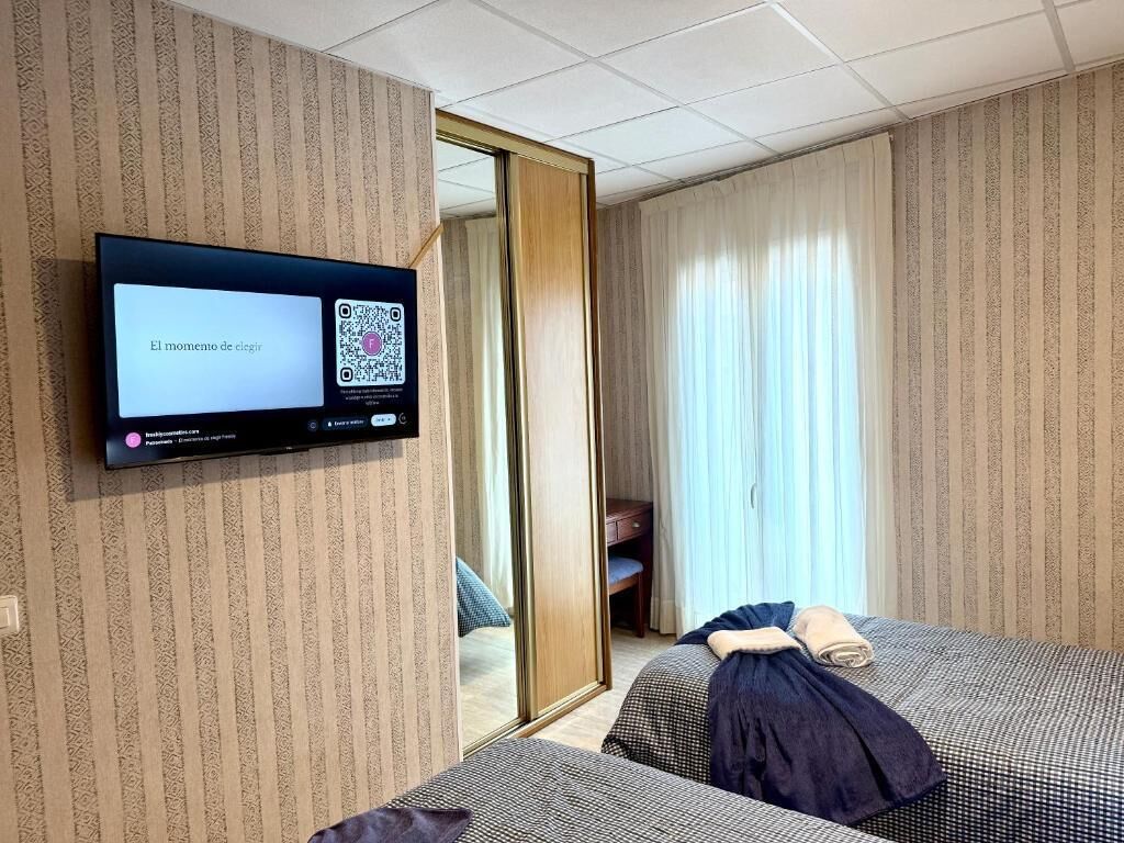 Hotelkamer met twee bedden, een aan de muur bevestigde televisie, een spiegel en een schuifdeur naar een badkamer.