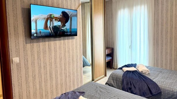Et hotelværelse med to senge, et fjernsyn, et spejl og en skydedør til en balkon.