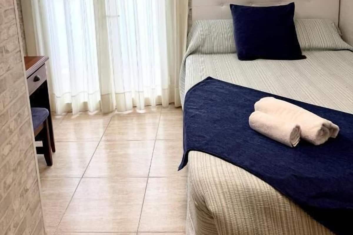 Una habitación de hotel con cama, escritorio, silla y ventana con cortinas.