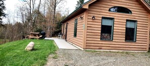 Een houten blokhut met een veranda, een picknicktafel en een steen op de voorgrond.